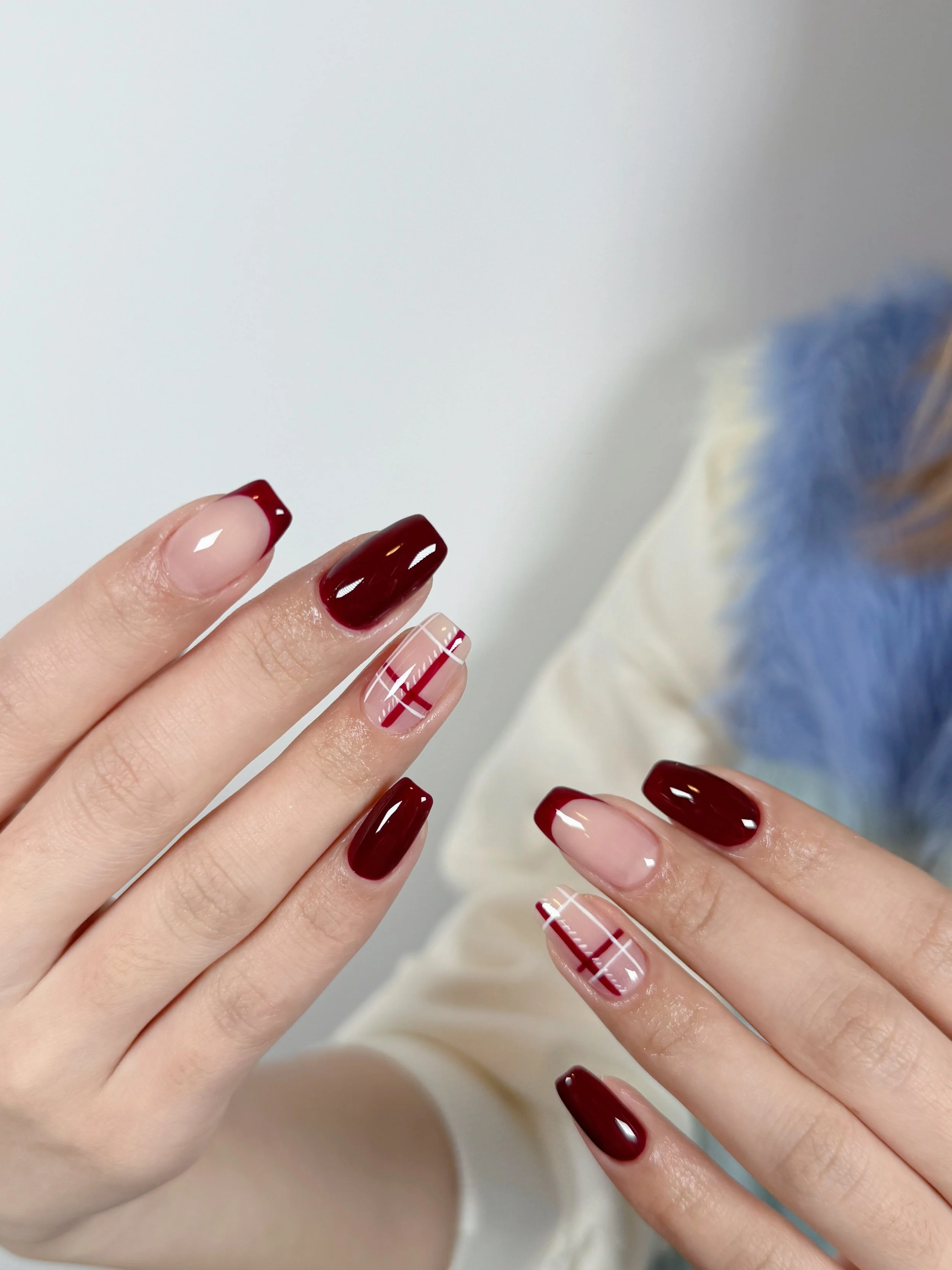 Close-up of hands with manicured nails in red, beige, and plaid design, held up against a plain background.