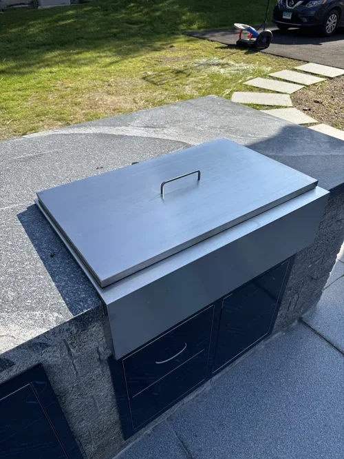 A stainless steel outdoor grill with a closed lid on a granite countertop, located on a patio area.