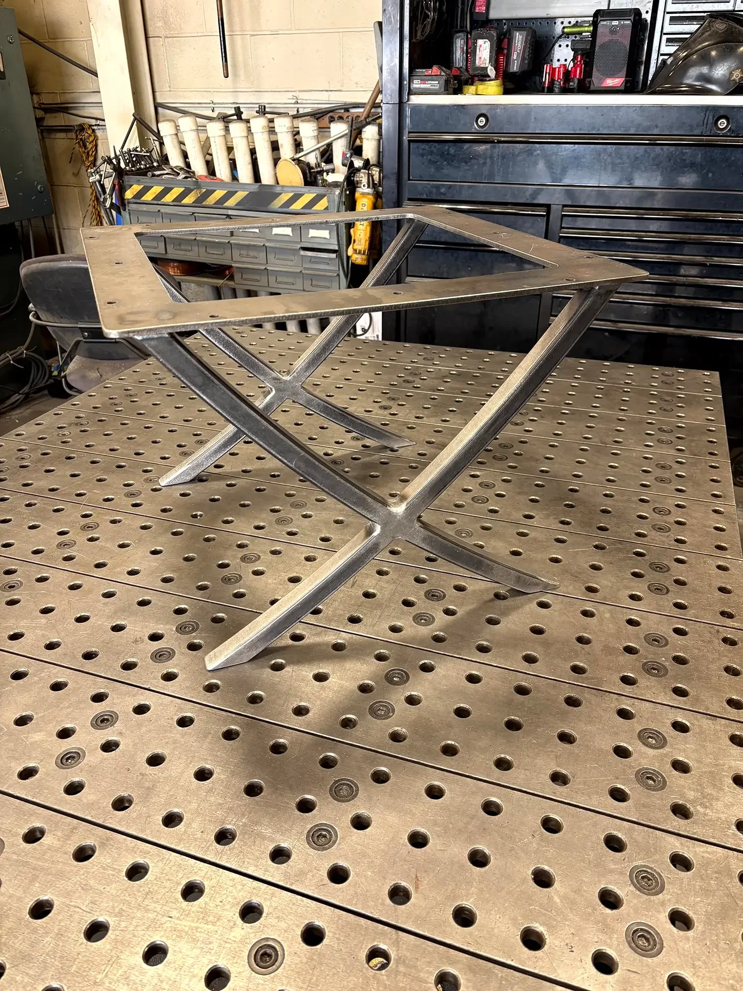 Metal frame assembly on a perforated worktable in a workshop, with tools and equipment in the background.
