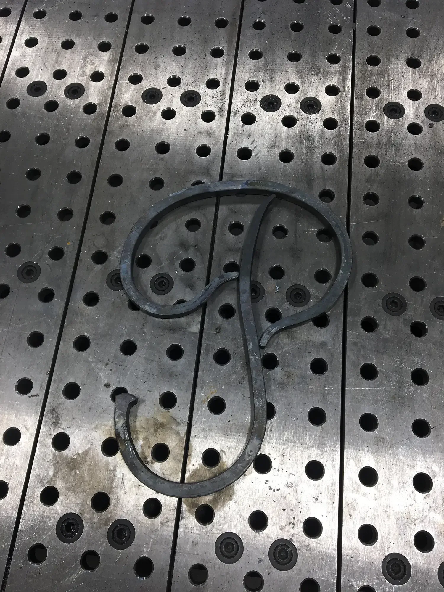 A metal surface with multiple circular holes and two metal rings lying on it.