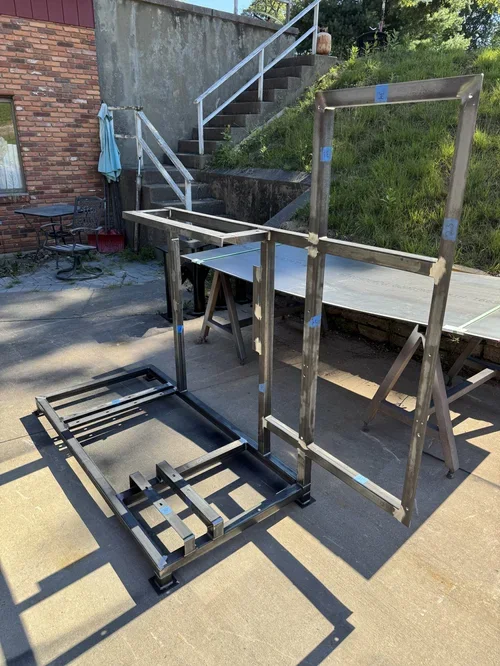 Metal frame structure outdoors on concrete, with stairs, steps, and patio furniture in background.