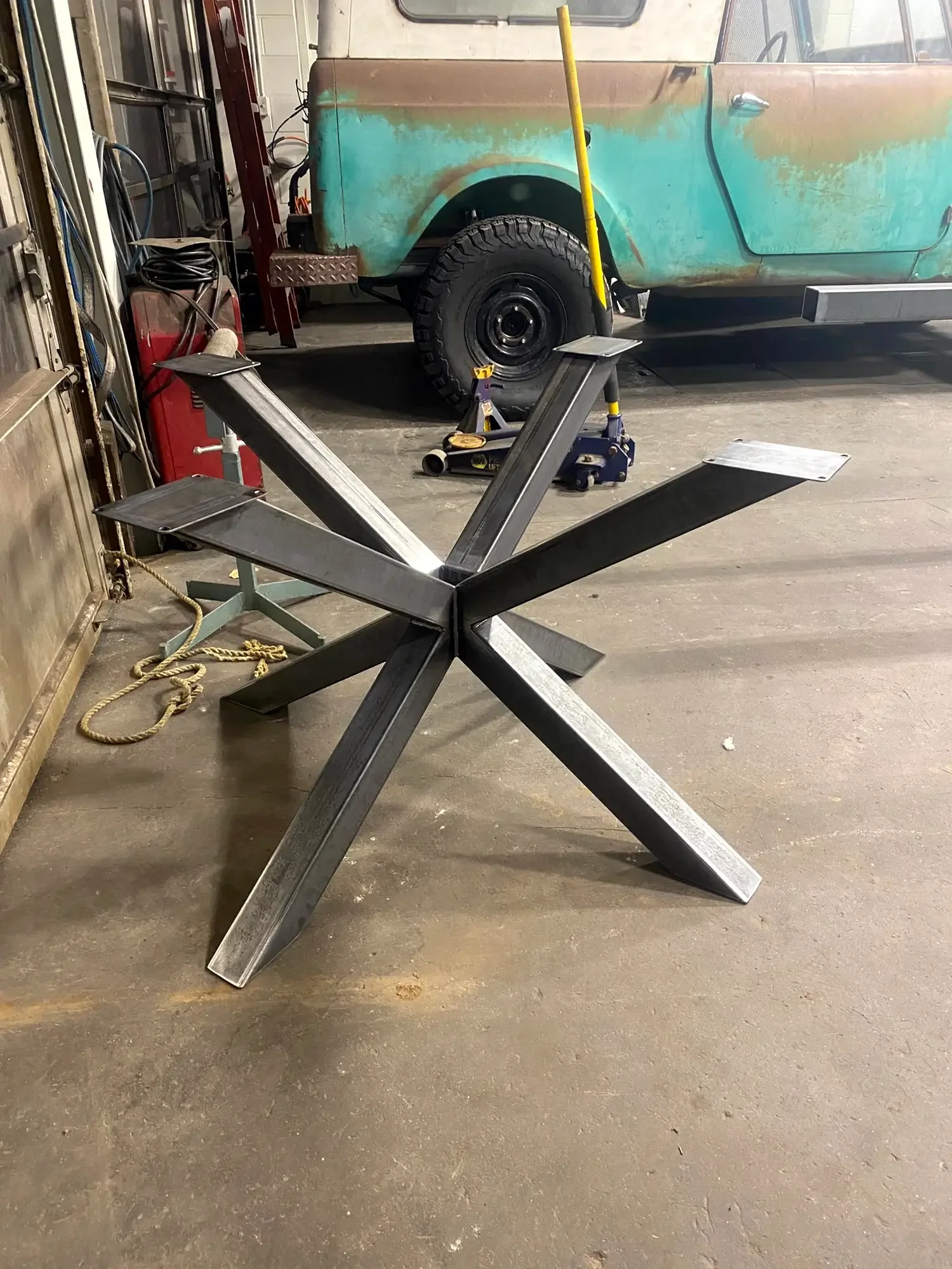 A metal frame structure on the floor in a garage or workshop with tools and a vehicle in the background.
