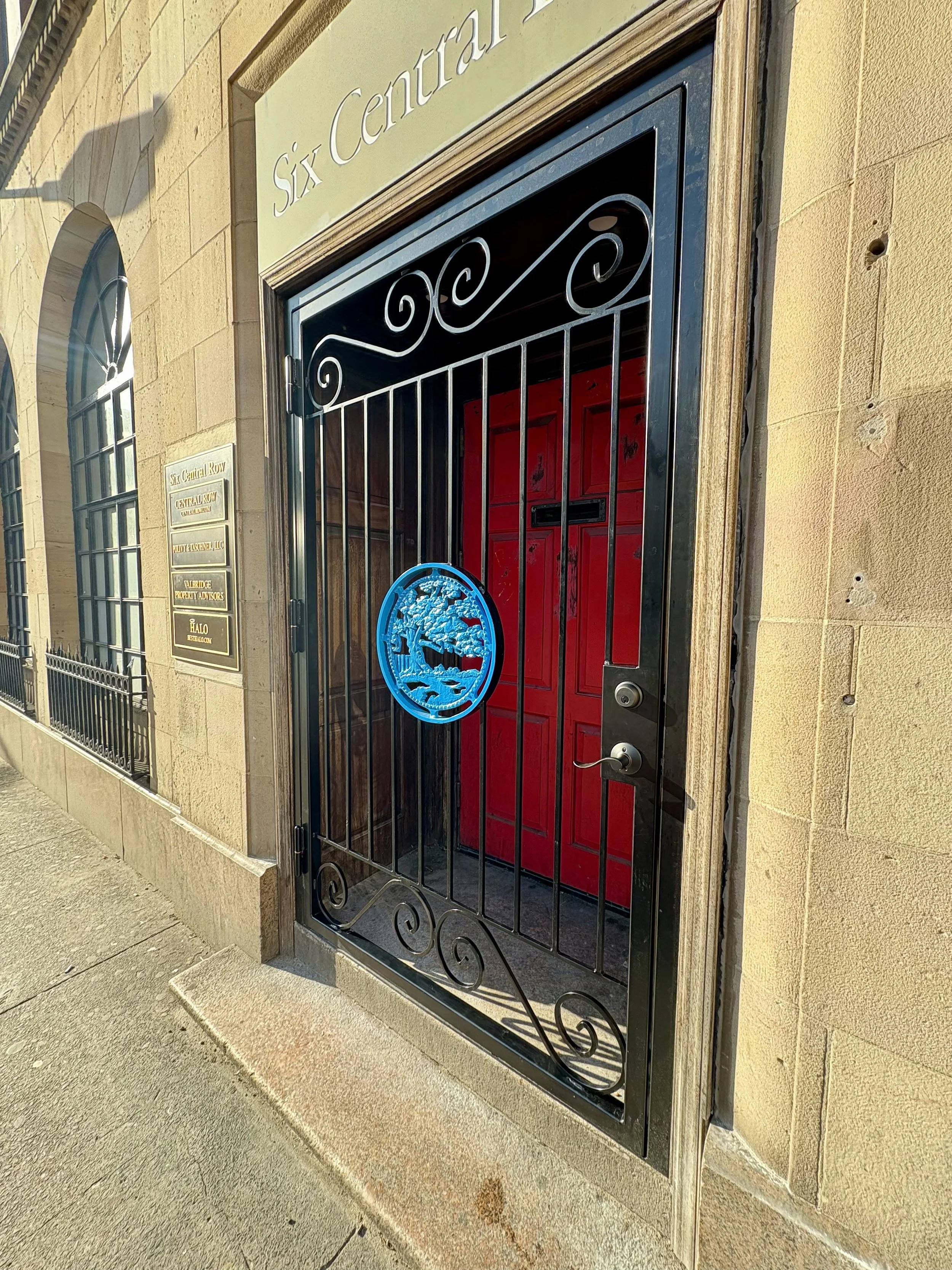 Entrance door with black metal gate and a blue logo, building labeled 'Six Central Row' with gold signage.