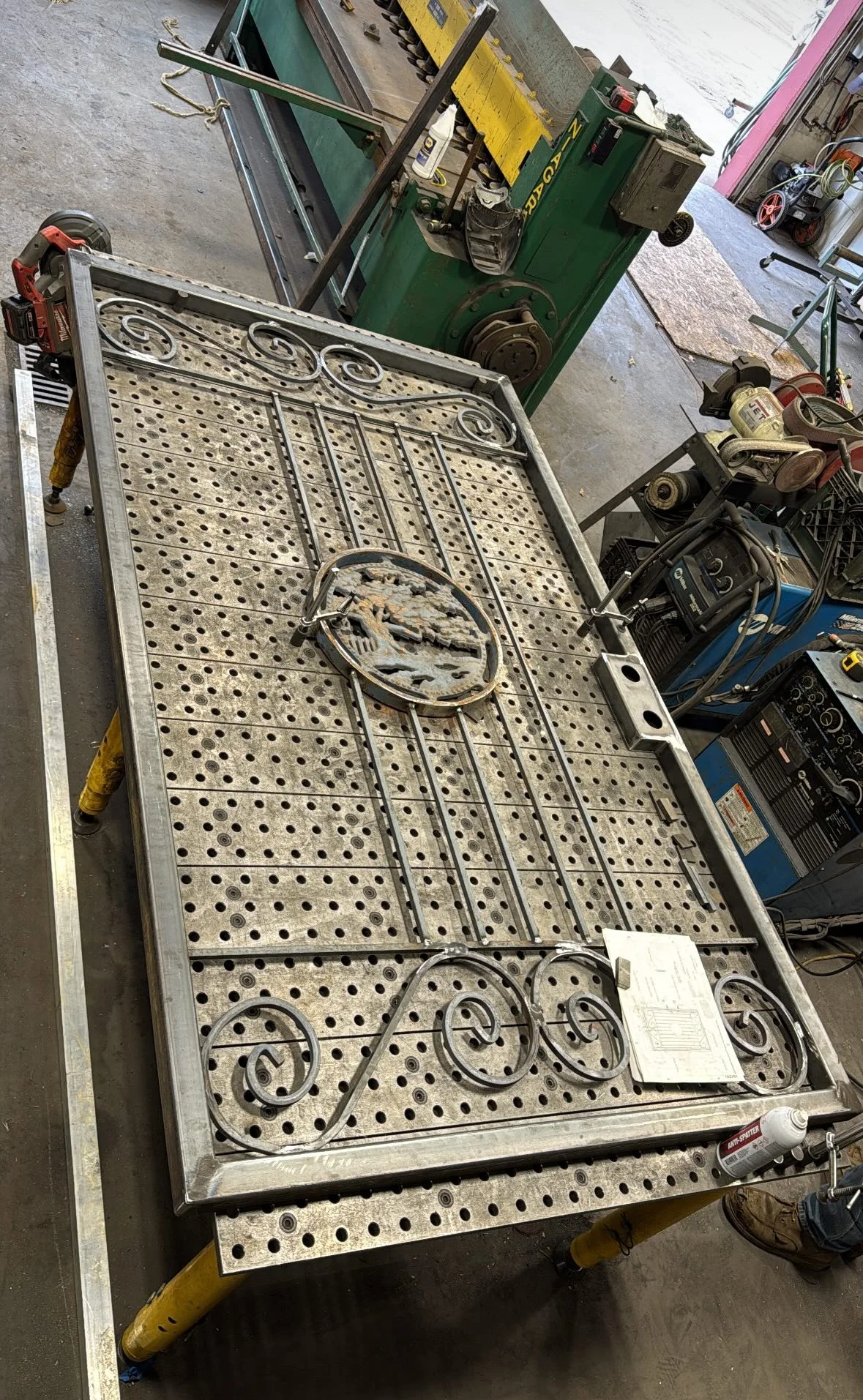 A metal worktable with a decorative wrought iron piece attached, in a workshop surrounded by tools and equipment.