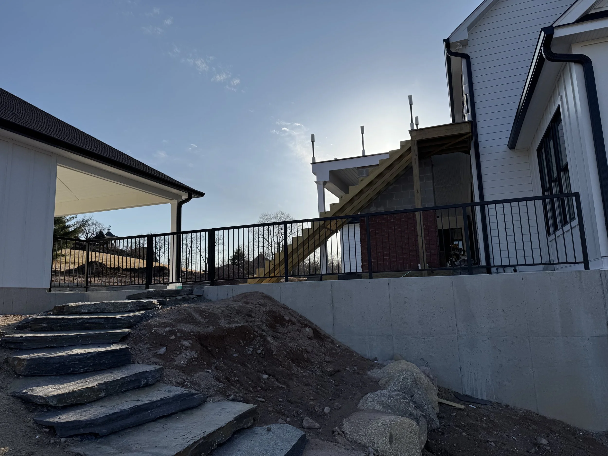 Construction site with stairs and a retaining wall next to a white house under a clear sky.
