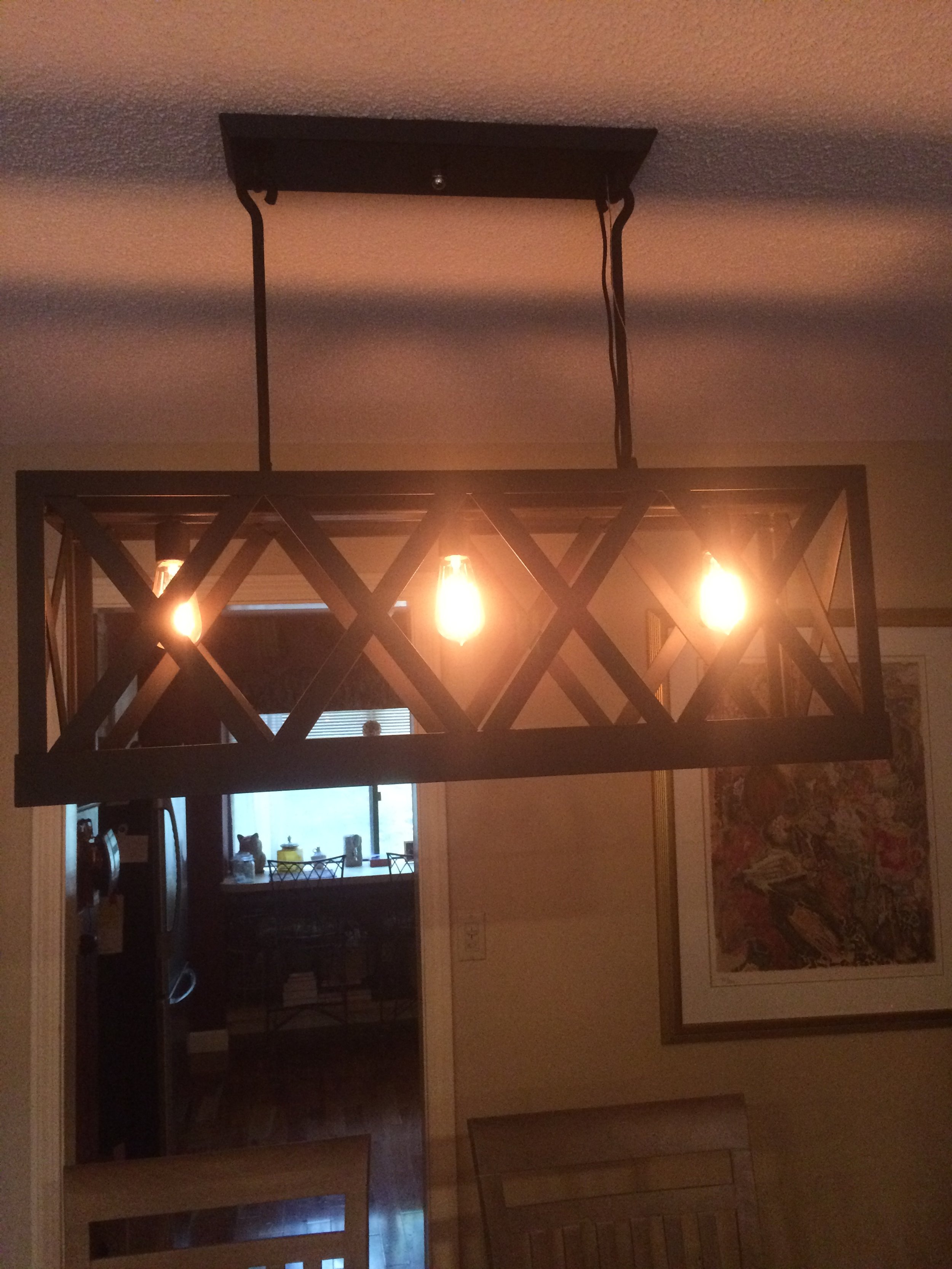 A rectangular black metal chandelier with three exposed light bulbs hangs from the ceiling over a dining table.