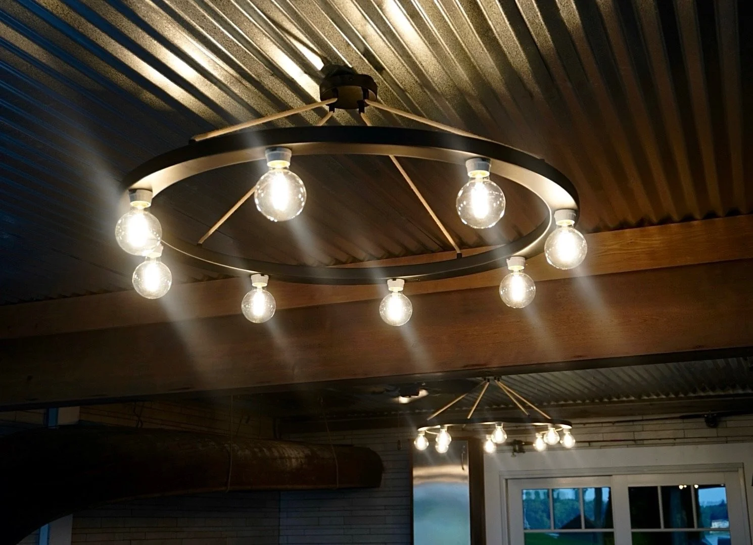 Modern ceiling light fixture with multiple exposed bulbs, hanging from a black circular frame attached to a dark wooden ceiling.