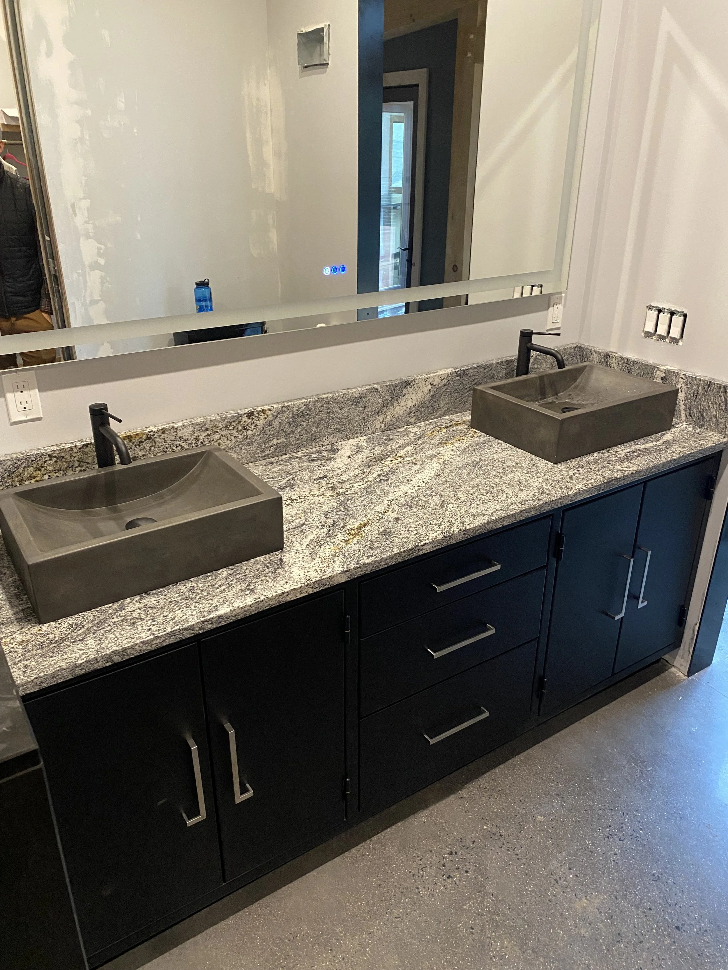 Modern bathroom vanity with two vessel sinks, black cabinets, and a large mirror.