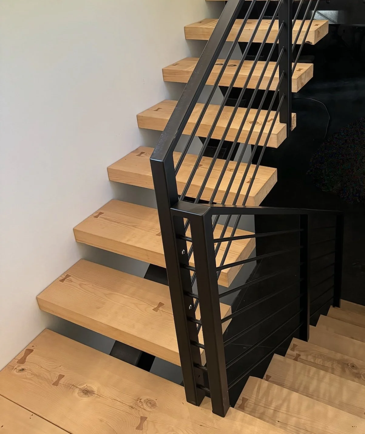 Wooden staircase with black metal railing on a white wall.