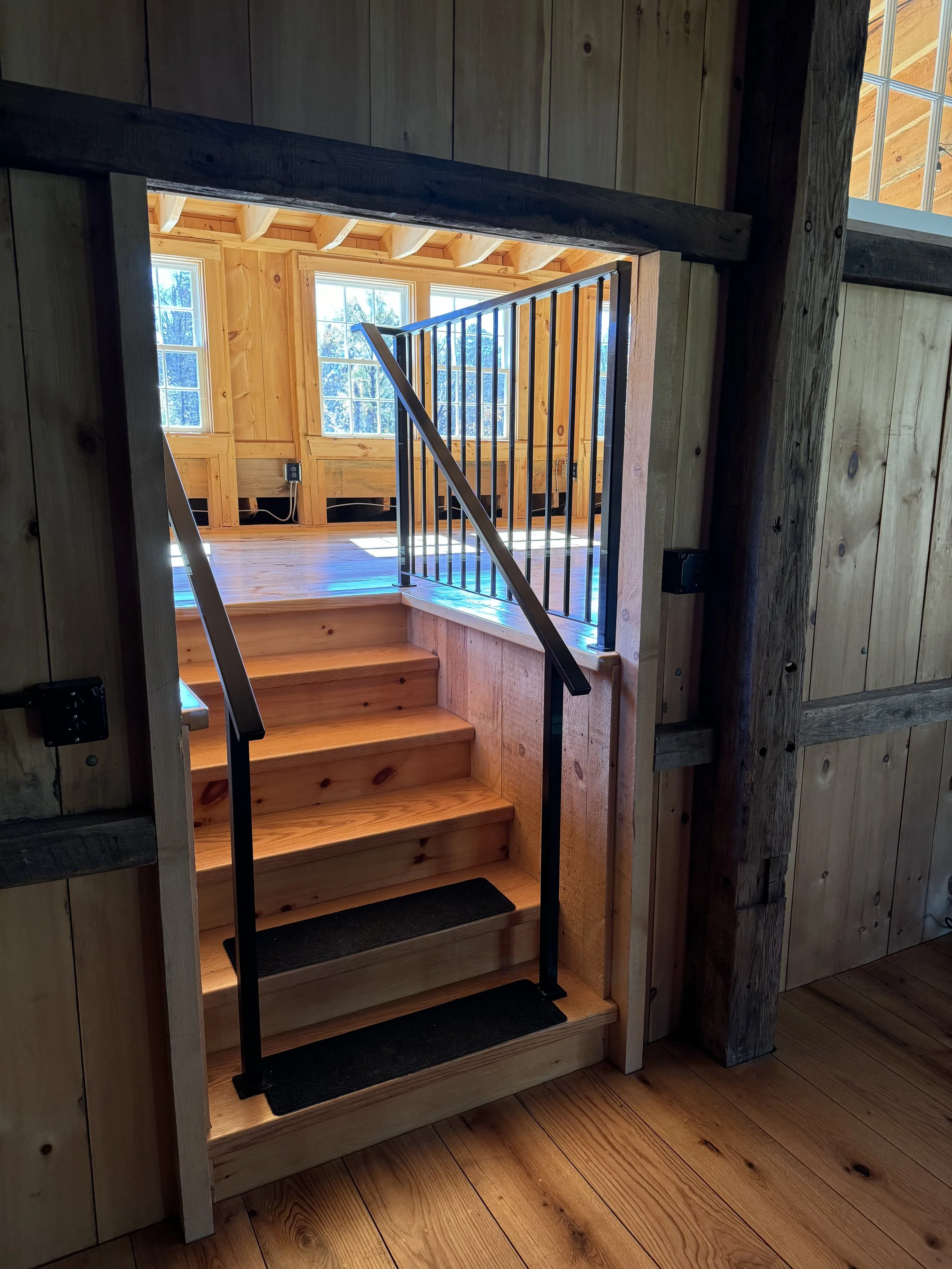 Wooden staircase leading to a bright room with large windows and wood-paneled walls.