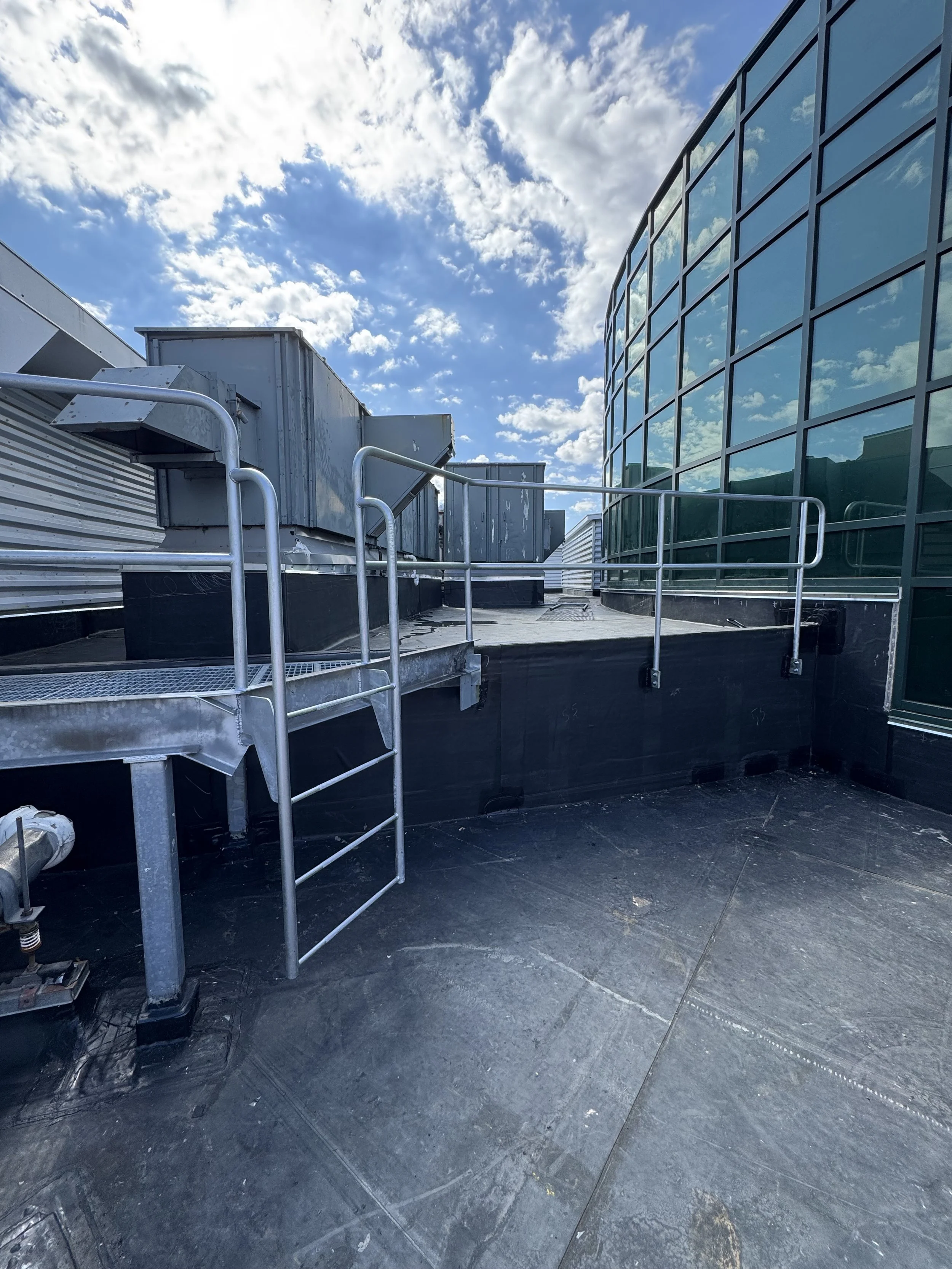 Rooftop with metal railings, glass windows on the right, and a partly cloudy sky overhead.