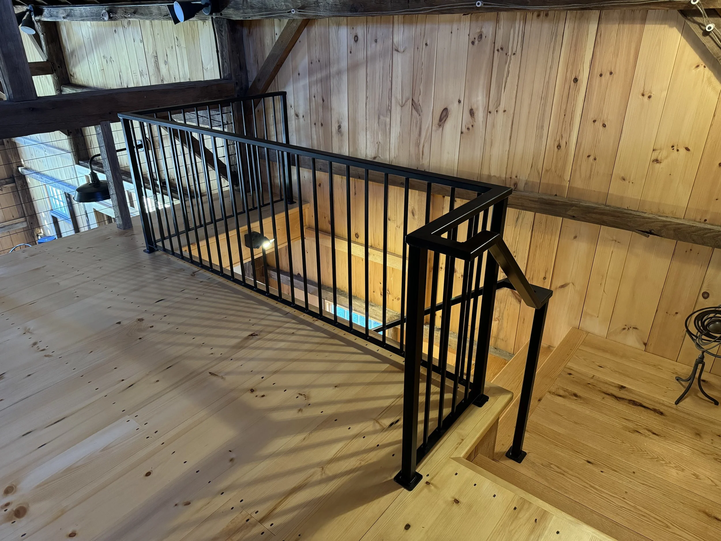Wooden staircase with black metal railing leading to a lower level in a rustic wood interior.