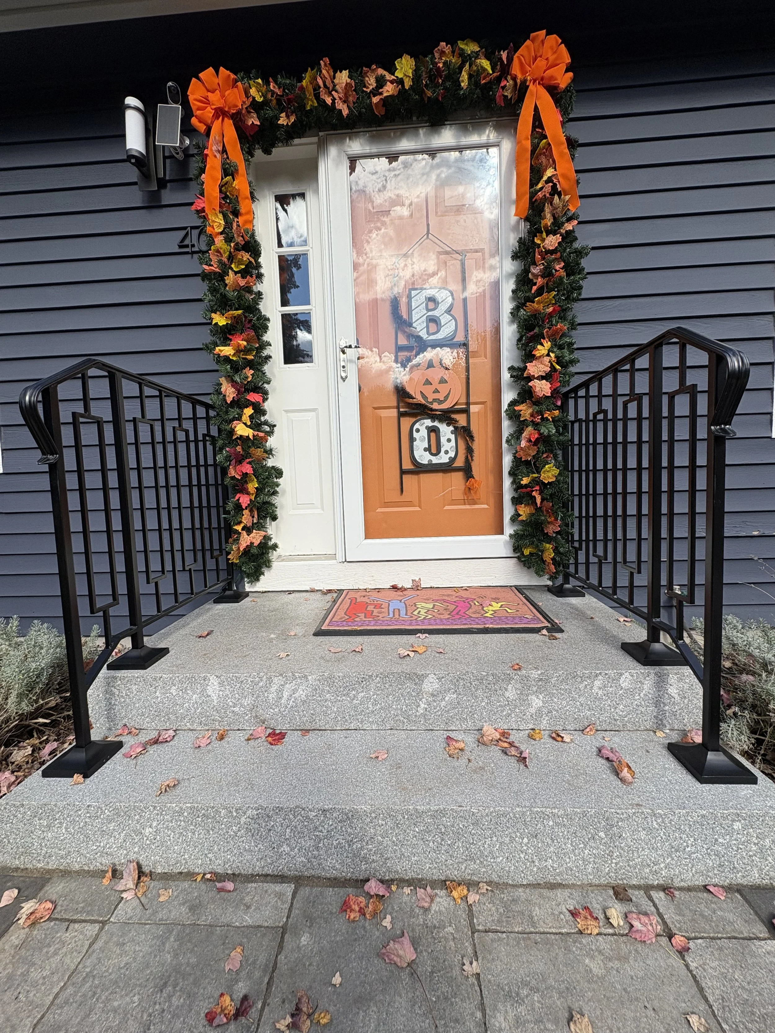 Front porch decorated for Halloween with fall leaves, a wreath, and a welcome mat.
