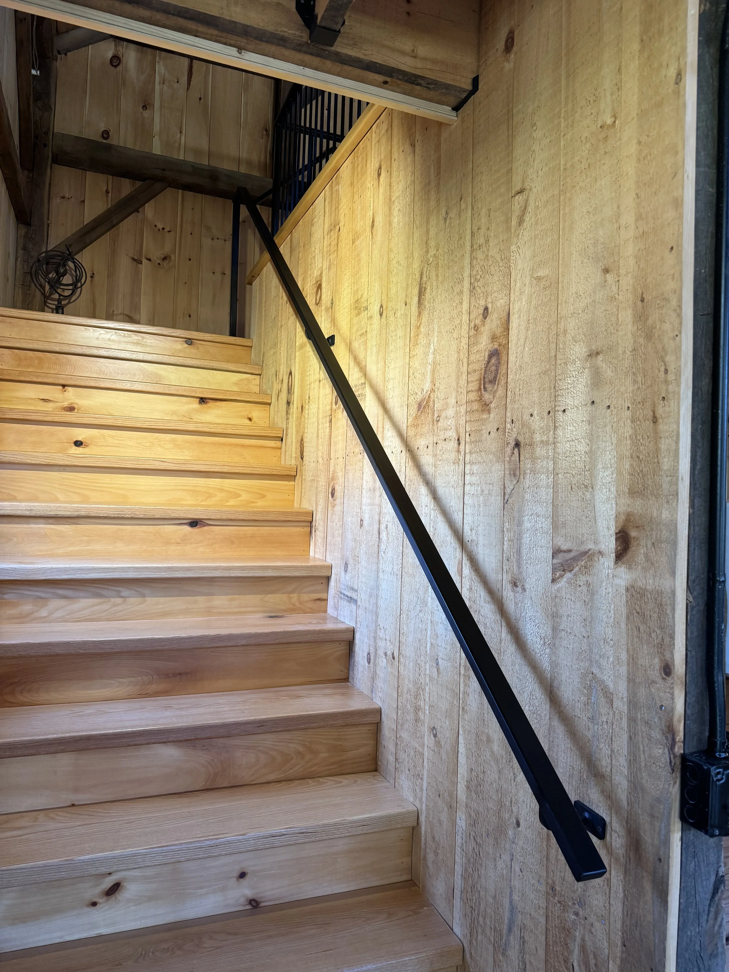 Wooden staircase with a black handrail, adjacent to wood-paneled wall inside a building