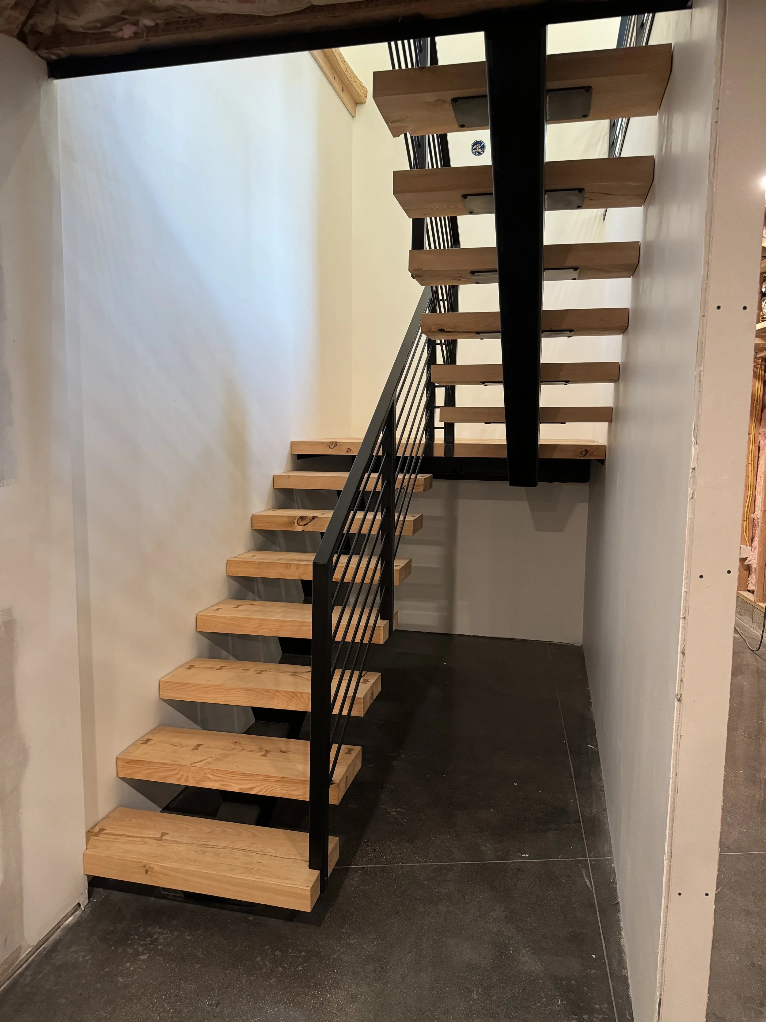 An unfinished staircase with wooden steps and black metal railings in a partially constructed space.