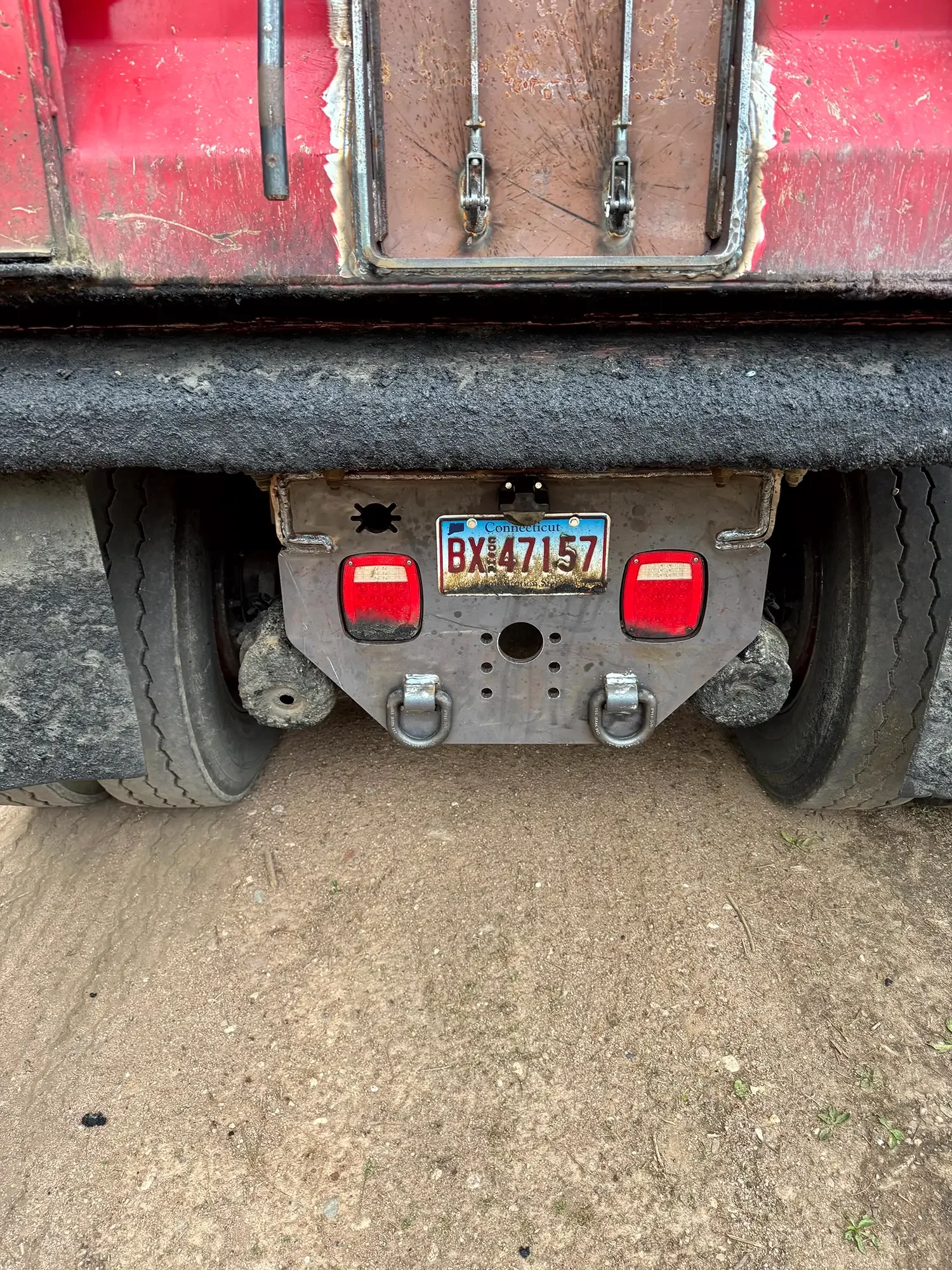 A close-up of the rear of a large construction truck showing the rear bumper, license plate from Connecticut, and some dirt on the tires and ground.