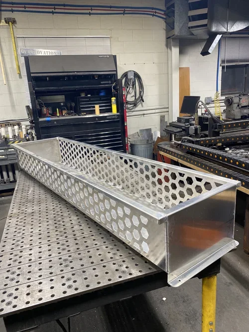 A metallic, elongated, rectangular object with honeycomb pattern sides on a workbench in a workshop.