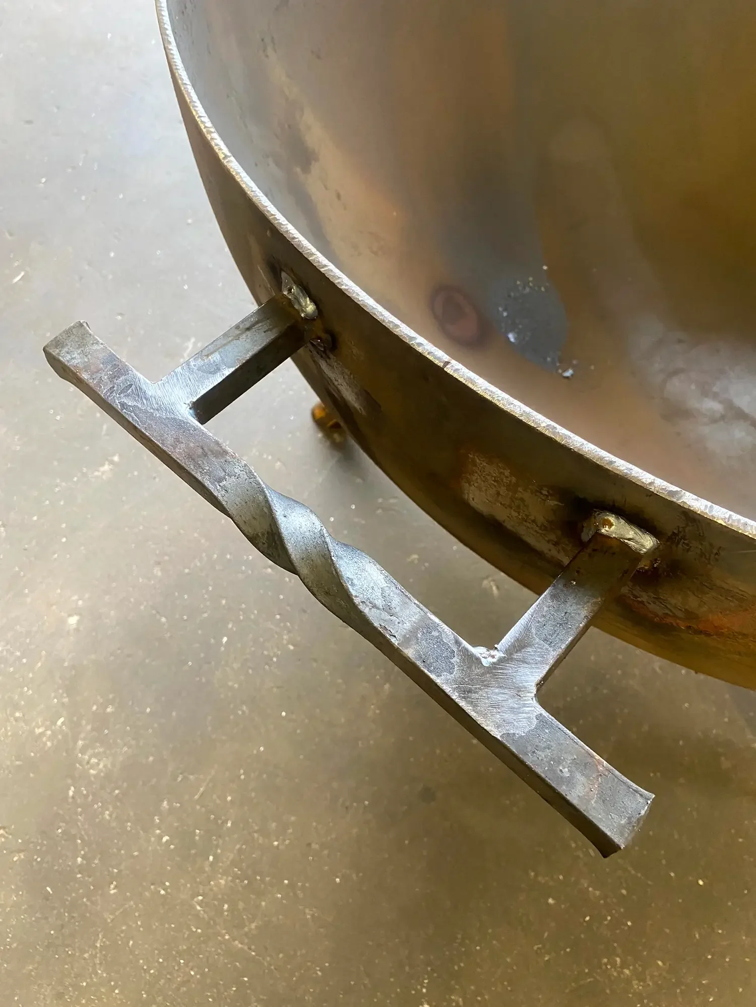 Close-up of metal bowl on metal stand, with reflections and a cloudy sky visible on the surface of the bowl, on a concrete floor.