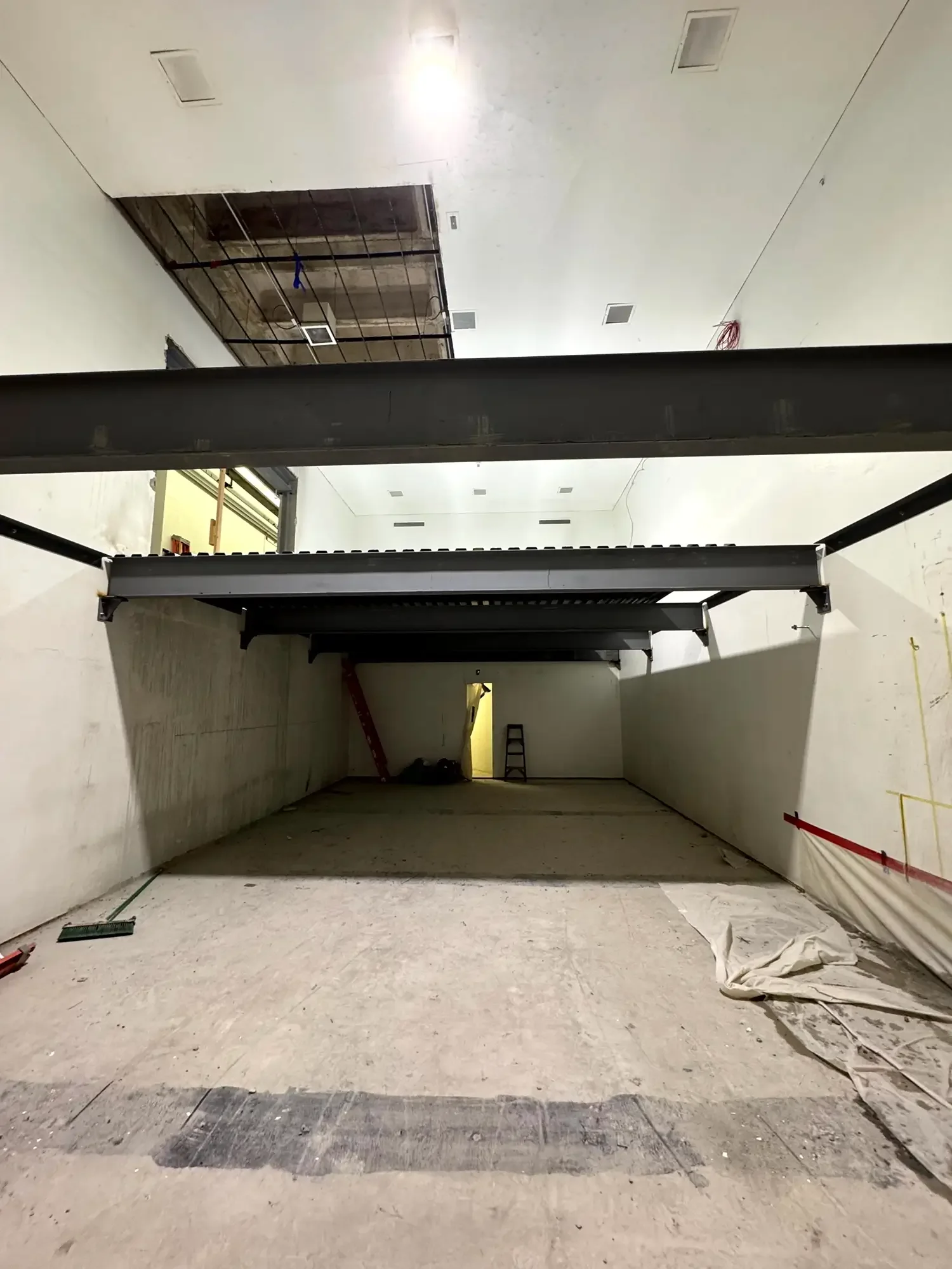Empty room under construction with a large open doorway and a metal above structural element, construction tools, and debris on the floor.