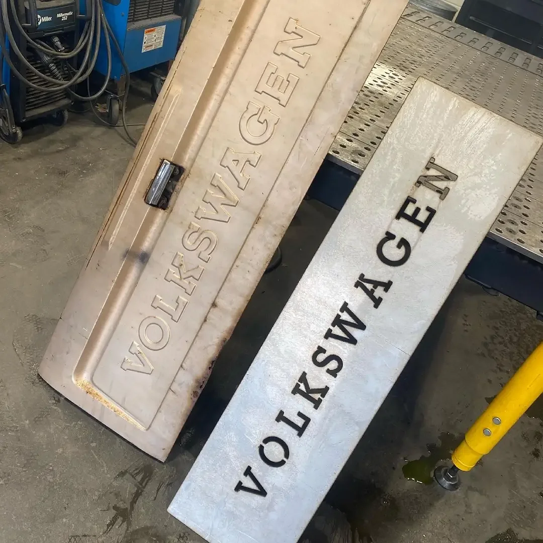 Two metal signs with embossed and painted text. One reads 'WASHEY GEVN' and the other is upside down and reads 'NVC WESG YAW'.
