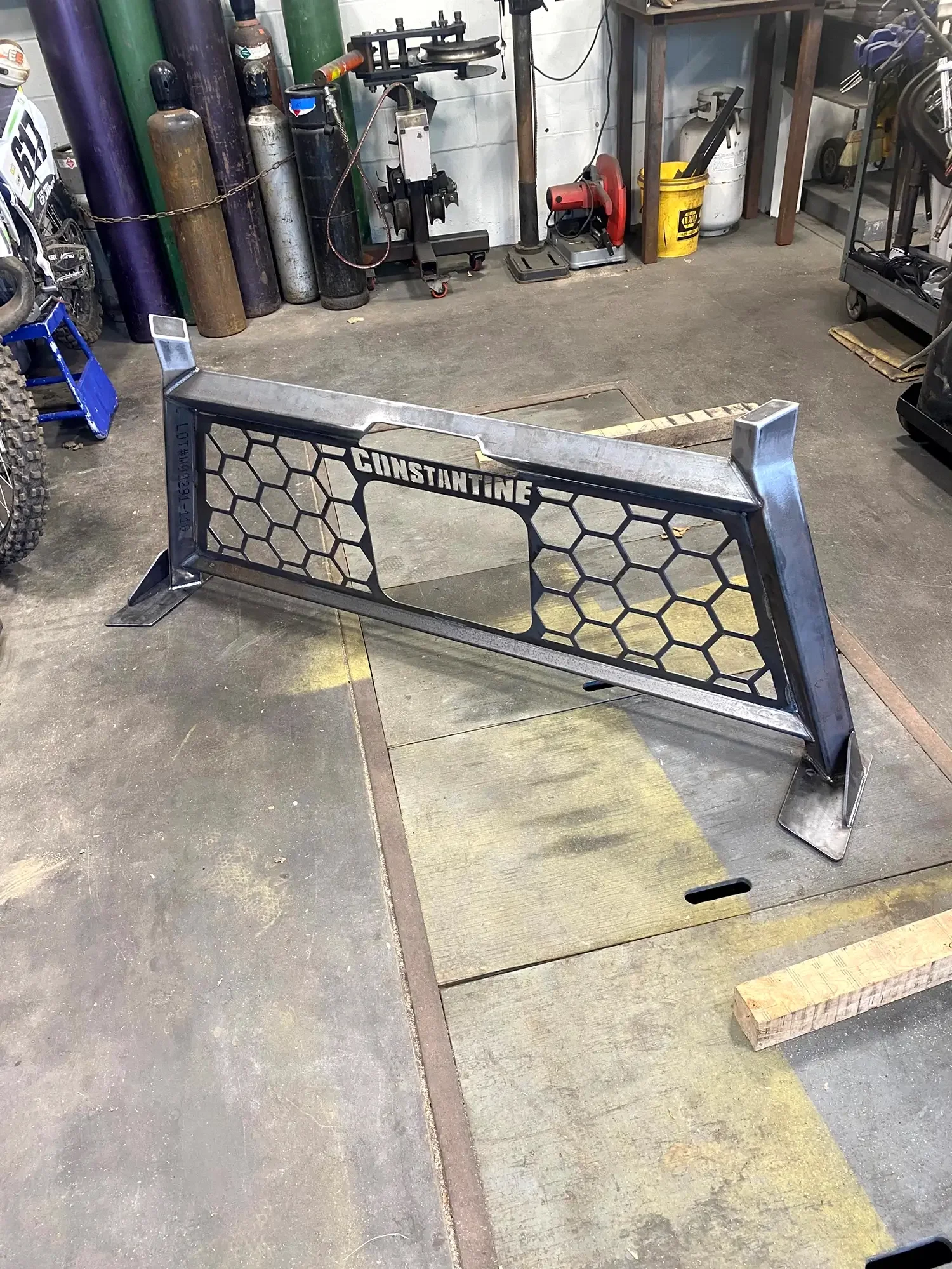 A metal racing bumper with the name CINDANTINE, in a workshop with gas tanks, tools, and equipment in the background.