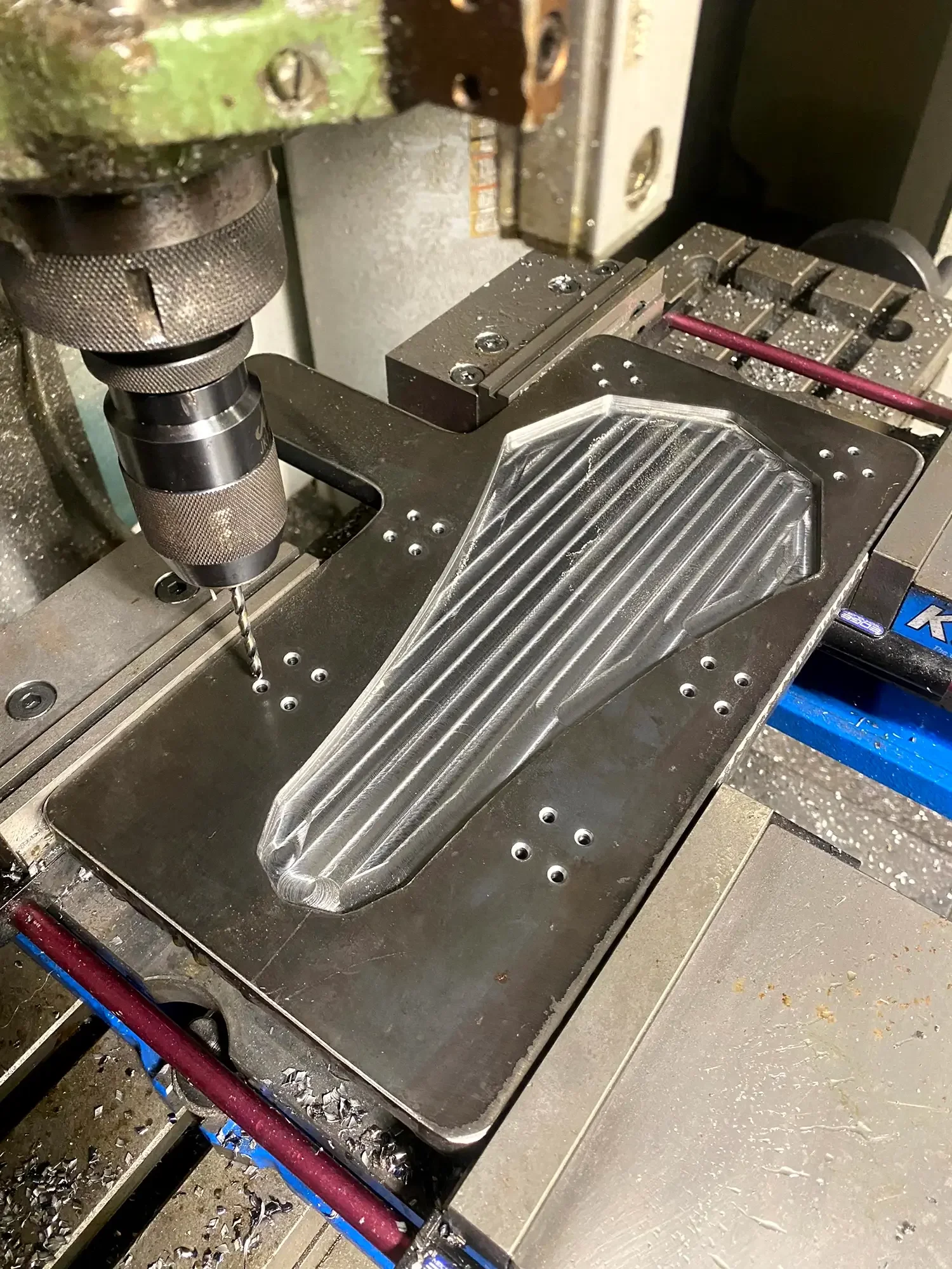 A computer numerical control (CNC) milling machine with a metal workpiece being milled. Metal shavings are scattered around the machine and on the work surface.