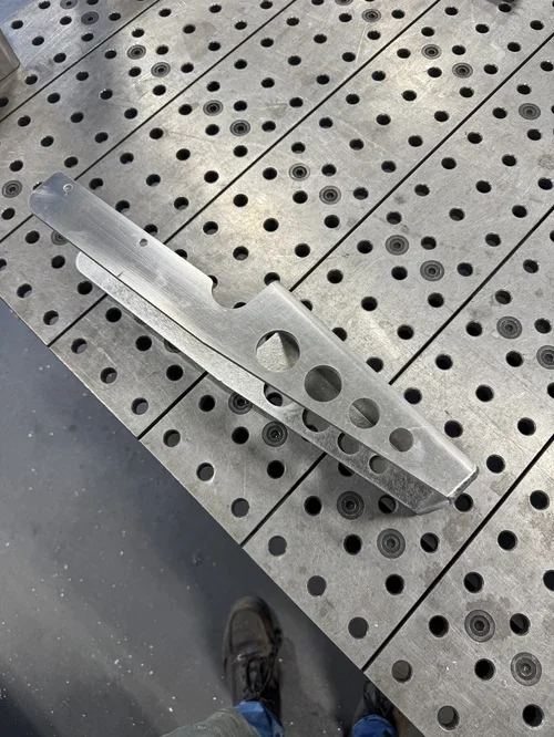 Metal piece with holes lying on a perforated metal surface.