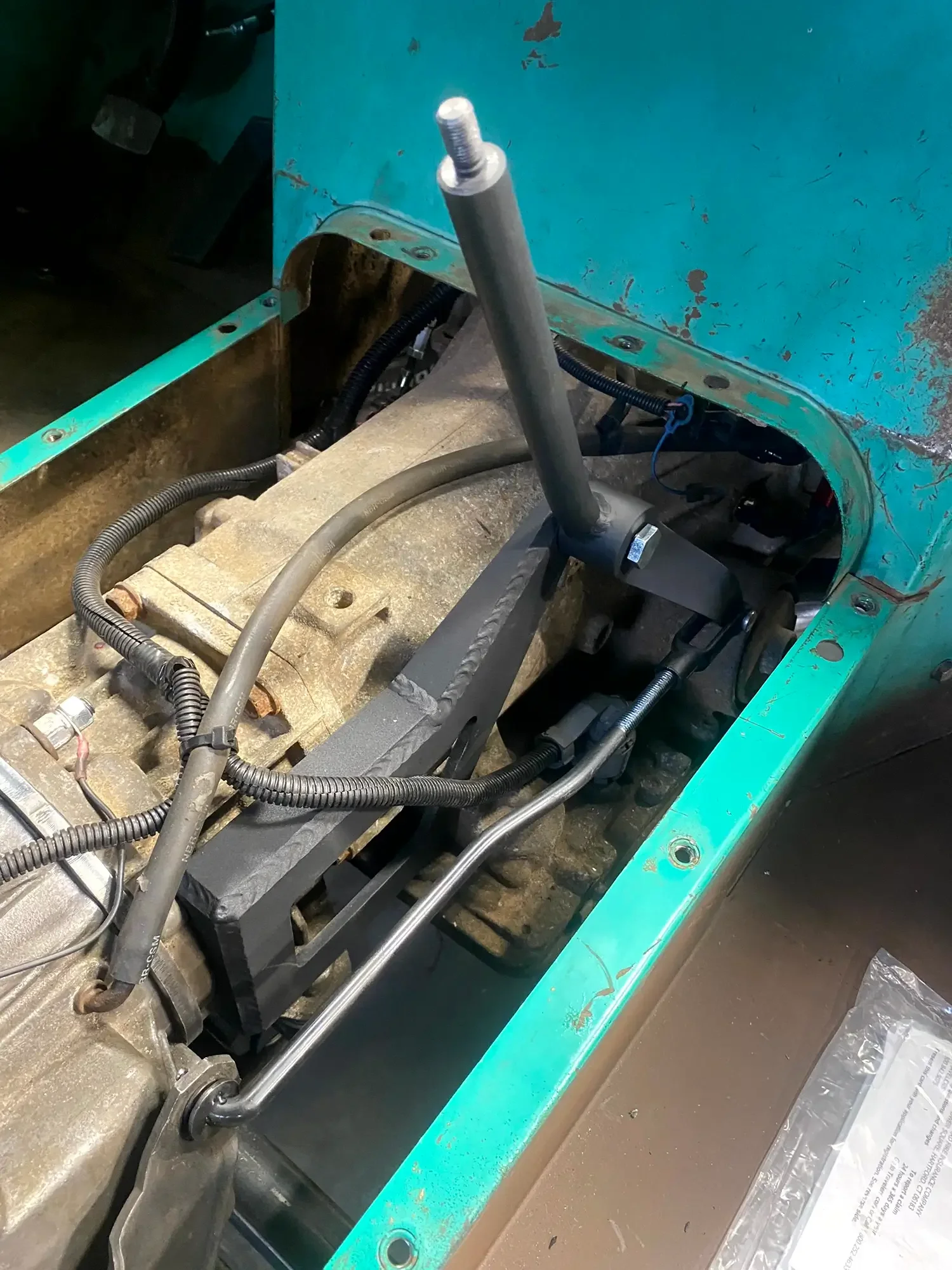 Close-up of an industrial machine with metal pipes, wires, and a mounting bracket, with a turquoise-colored metal housing in the background.