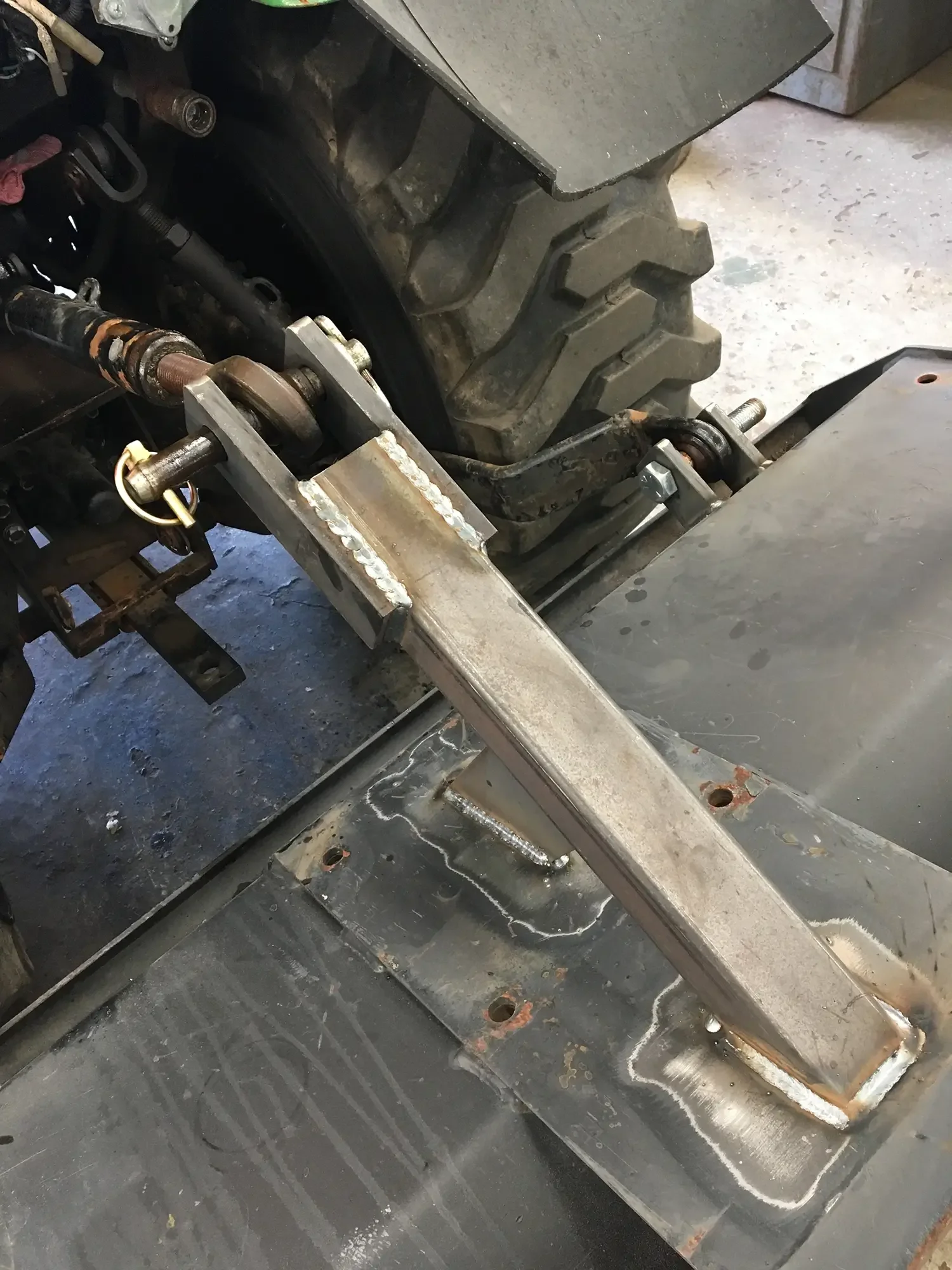 Close-up of a metal frame and machinery parts, with welding marks and bolts. The surface appears to be a workshop or construction site.