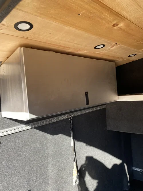 A stainless steel cabinet with a black handle, mounted below a wooden table, with three circular black and white recessed lights on the table's surface.