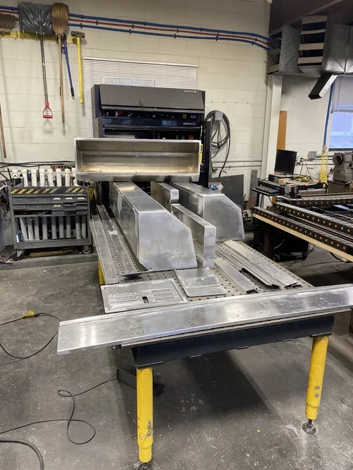 Industrial machine used for manufacturing or processing, with metal components and a conveyor system, situated in a workshop or factory setting.