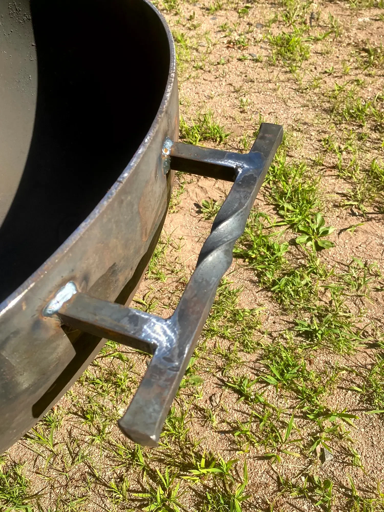 Close-up of a metal trampoline frame on a dirt ground with green grass patches.
