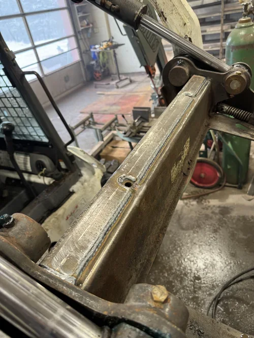 Close-up of a metal machine part in a workshop with tools, equipment, and a window in the background.