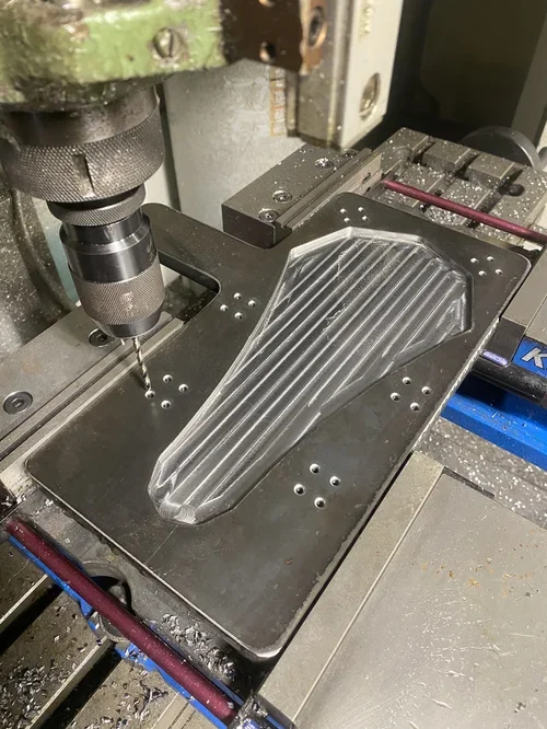 A CNC machine drilling into a metallic mold with a ribbed pattern.