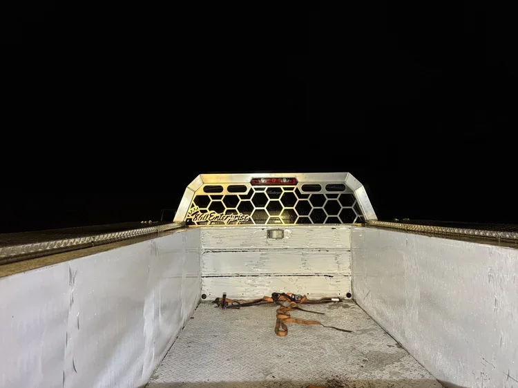 The bed of a pickup truck at night with a tow strap and hook on the floor, and a hexagon-patterned cargo barrier in the truck bed.