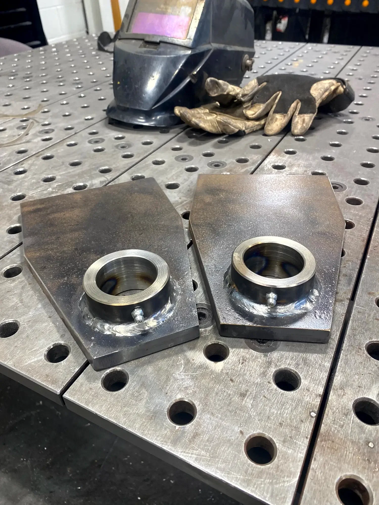 A metal welding or machining workbench with two metal blocks and a welding helmet or mask with a dirty glove resting on it.