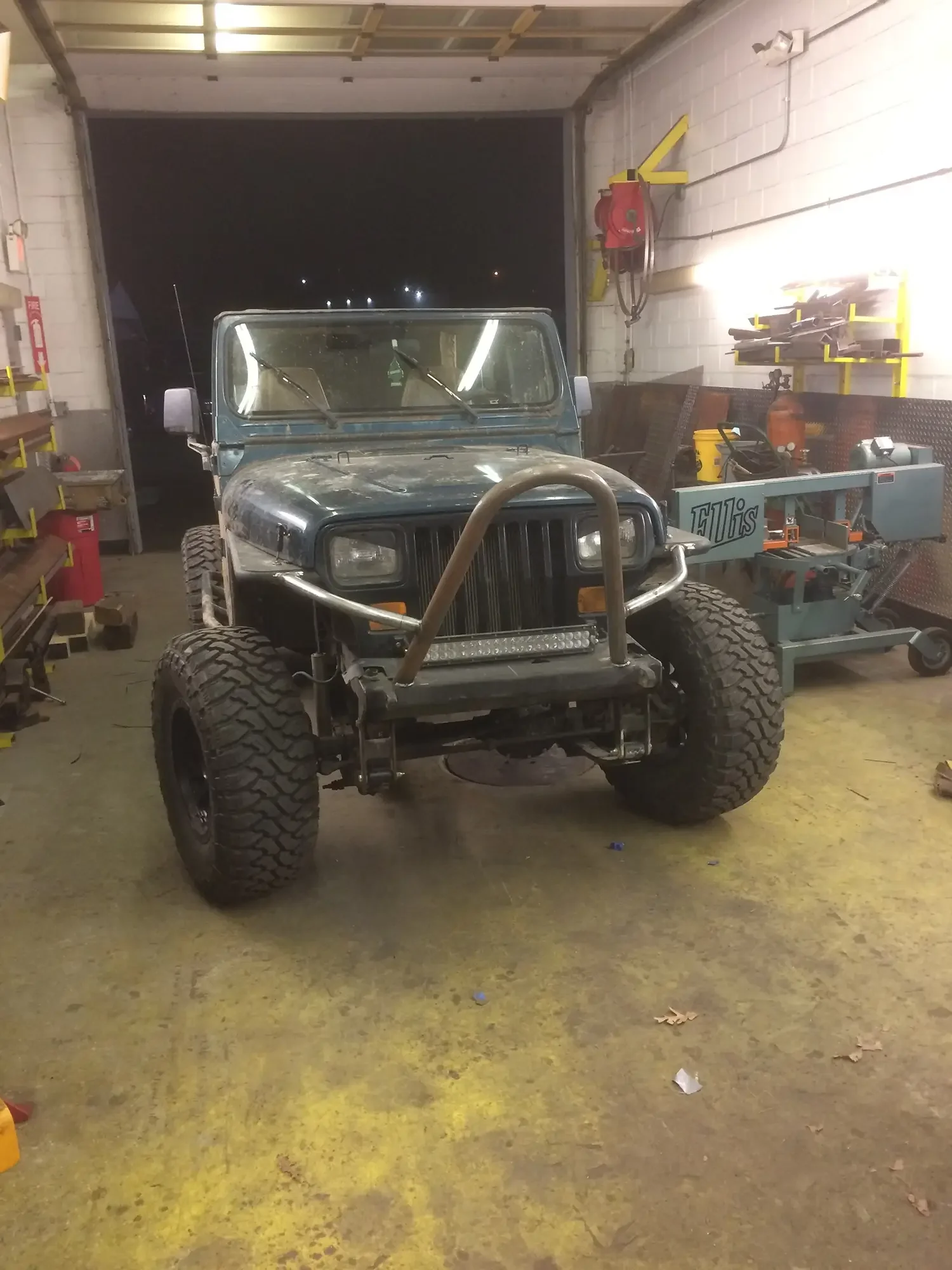 A rugged off-road vehicle inside a workshop or garage, with tools and equipment around, and a dark open garage door behind it.