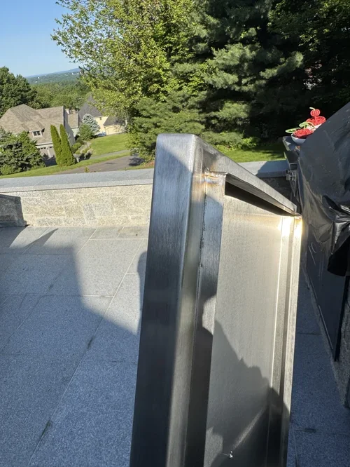 Metal handrail on a rooftop with trees, houses, and a cloudy sky in the background.