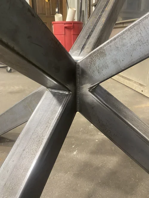 Close-up of welded metal beams forming a star-shaped intersection in a workshop.