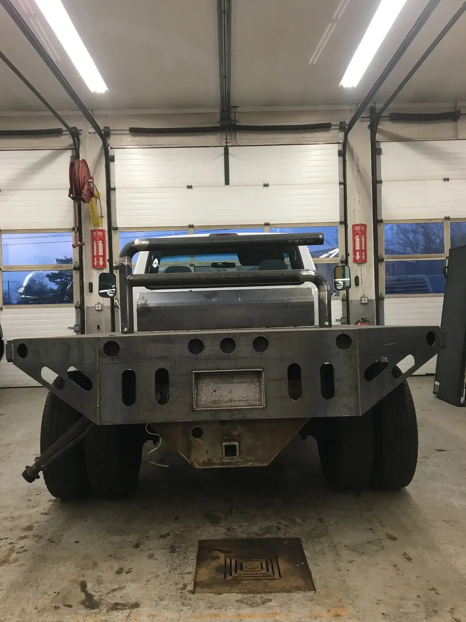 Front view of a flatbed truck inside a garage with white roll-up doors and fluorescent lights.