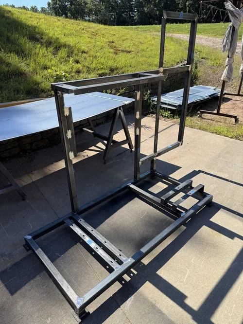 Metal frame structure on a concrete patio with a grassy hill and trees in the background.