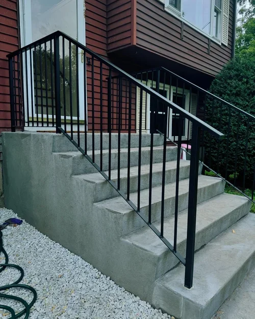 Concrete front steps with black metal handrail outside a residential building