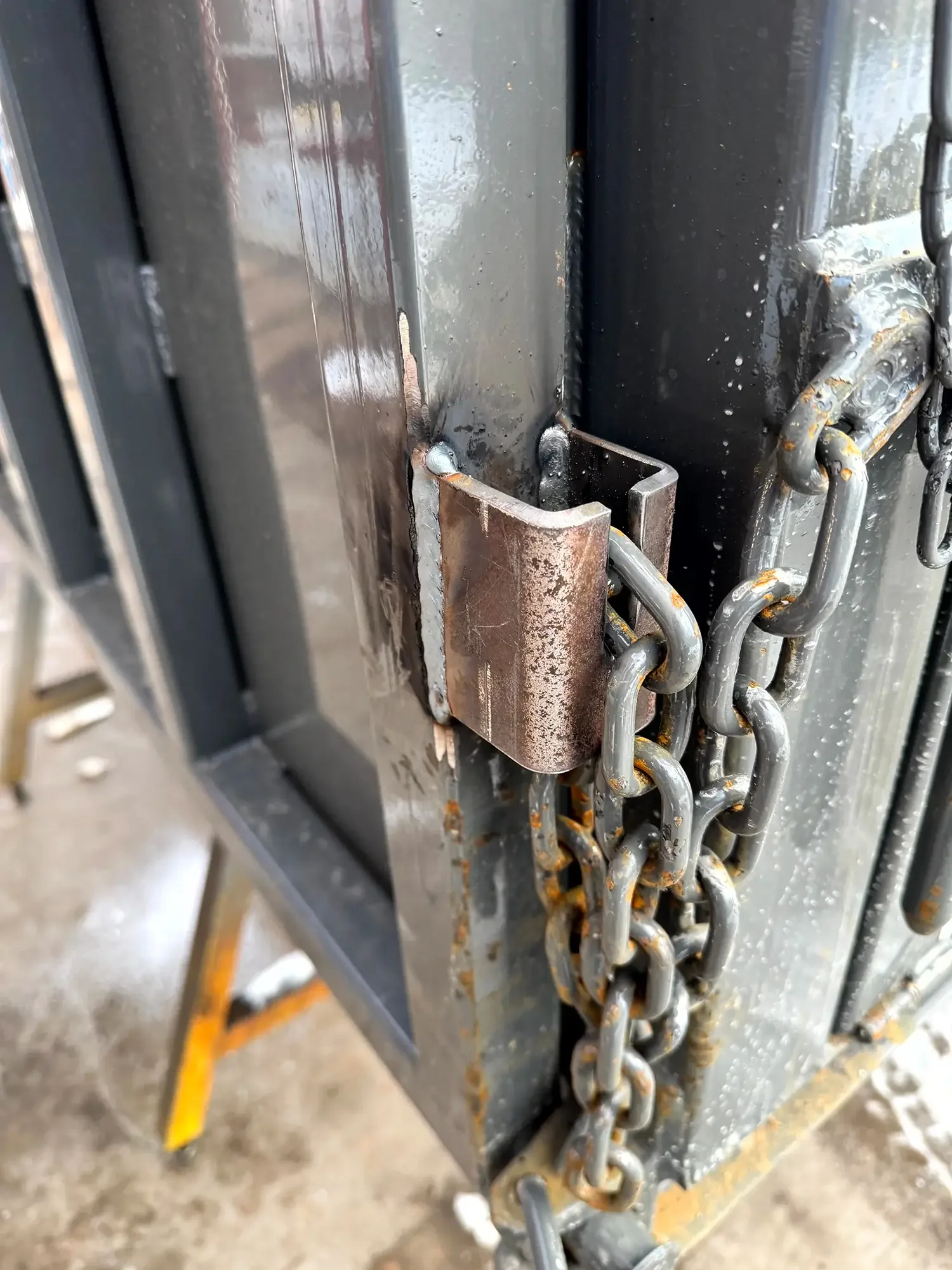 Close-up of a locked chain securing a metallic cabinet or safe with visible rust and welding.