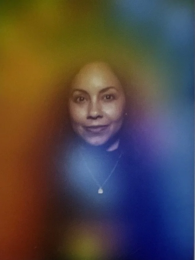 Veronica smiling, wearing a black top and a necklace, surrounded by a colorful, rainbow-like aura.