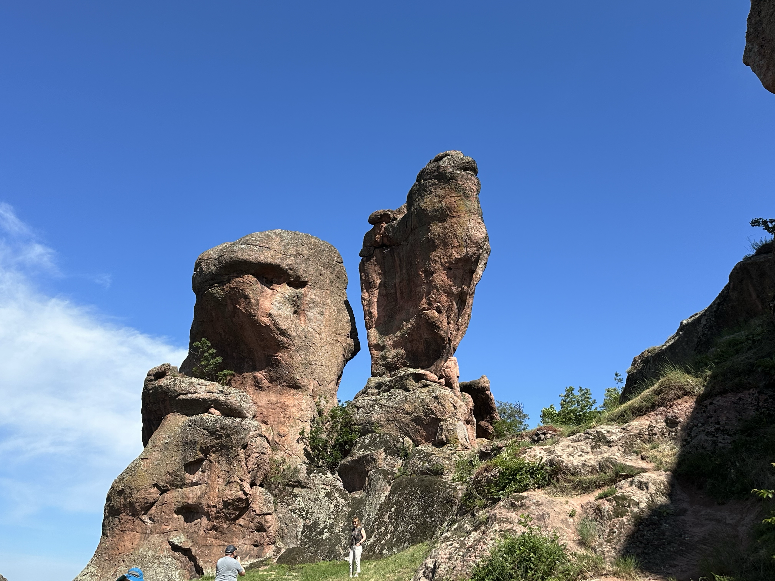 People standing on rocky terrain near large rock formations under a clear blue sky