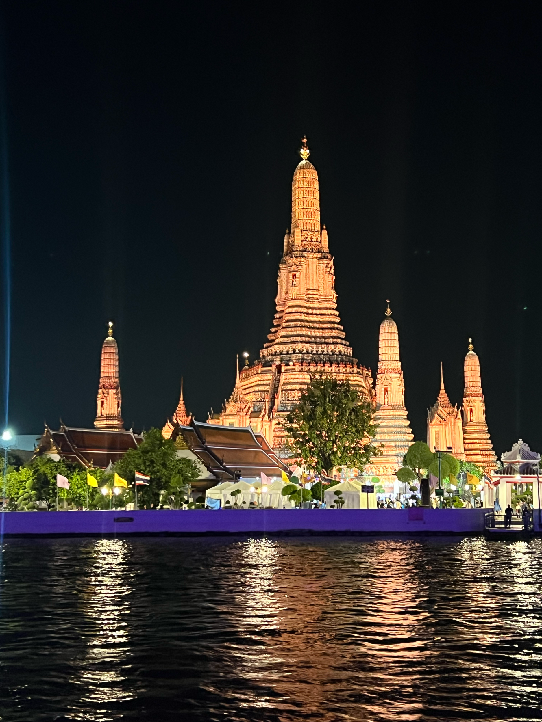 Night view of a historic temple or palace with tall spires, illuminated and reflecting in a body of water in the foreground.