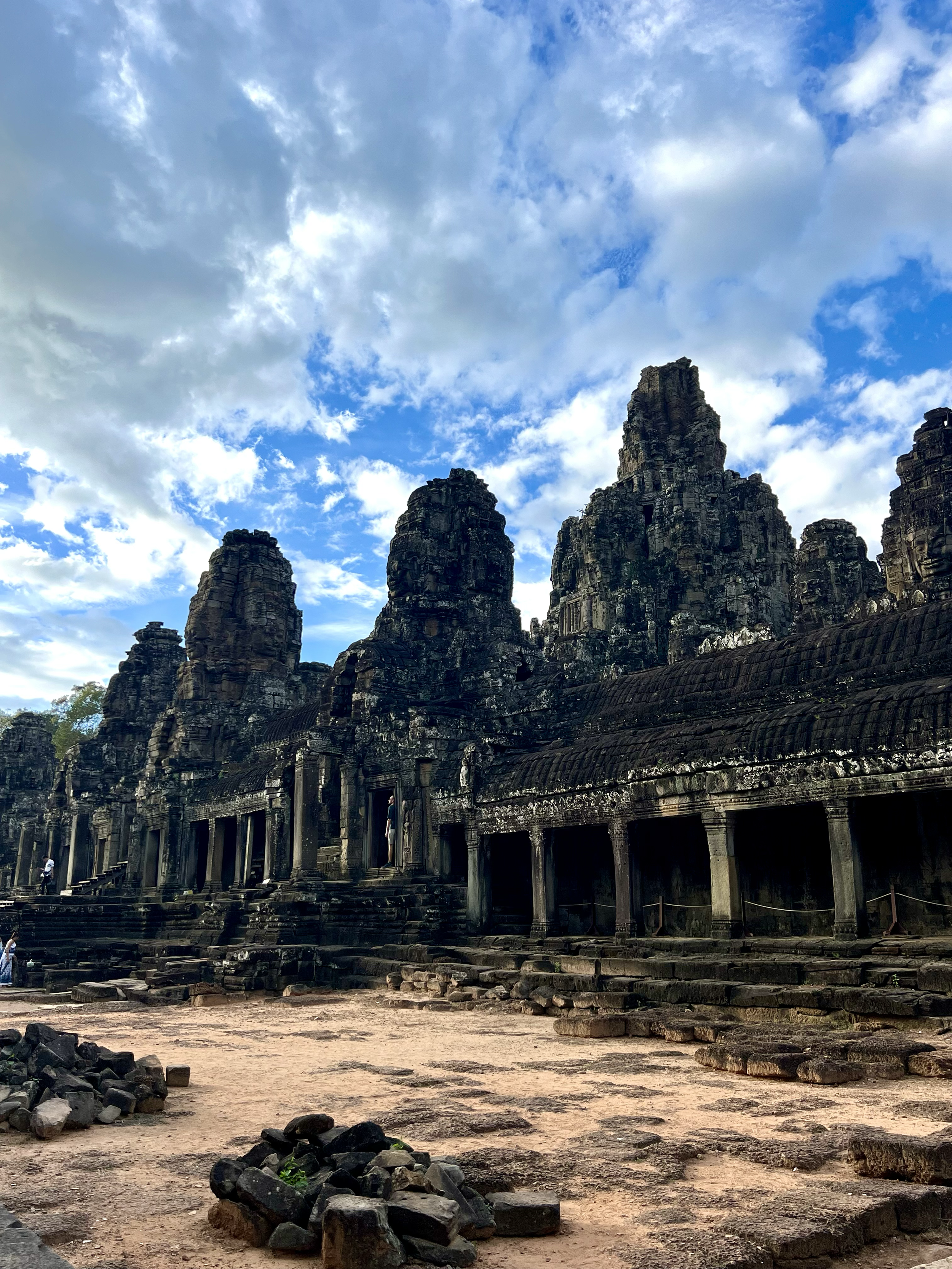 Ancient stone temple ruins with multiple towers against a partly cloudy sky with blue skies and white clouds.