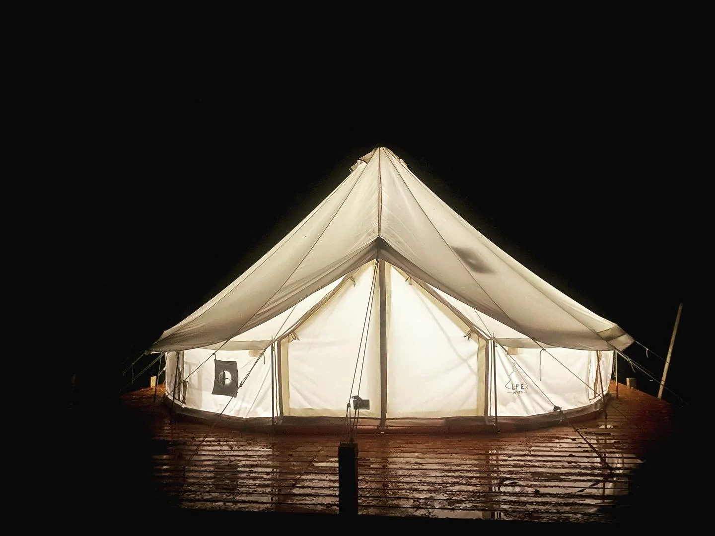 A lit up white tent on a wooden deck at night with a dark sky in the background.