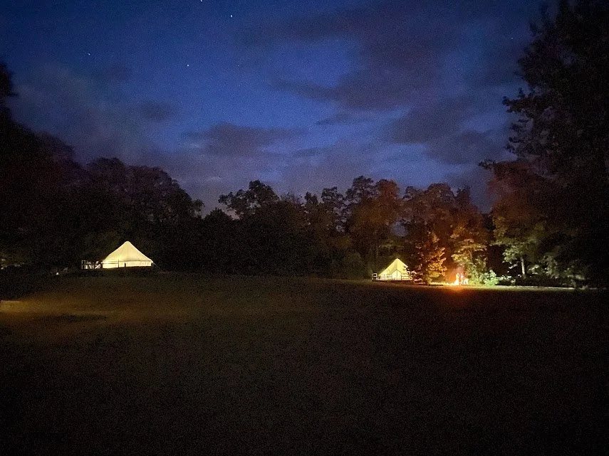 Nighttime scene with two illuminated tents and trees in the background under a dark sky.