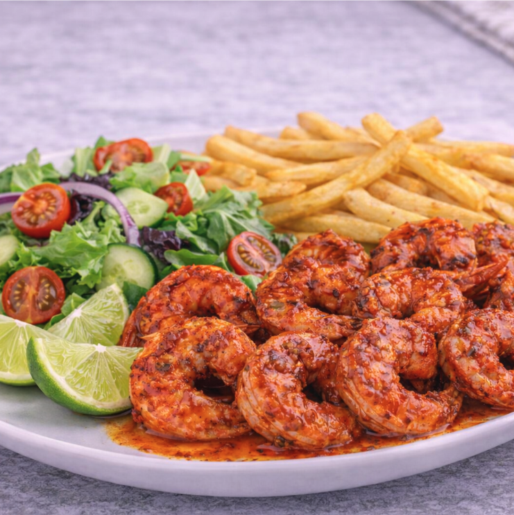 Shrimp in spicy sauce with side salad, French fries, and lime wedges on a white plate.